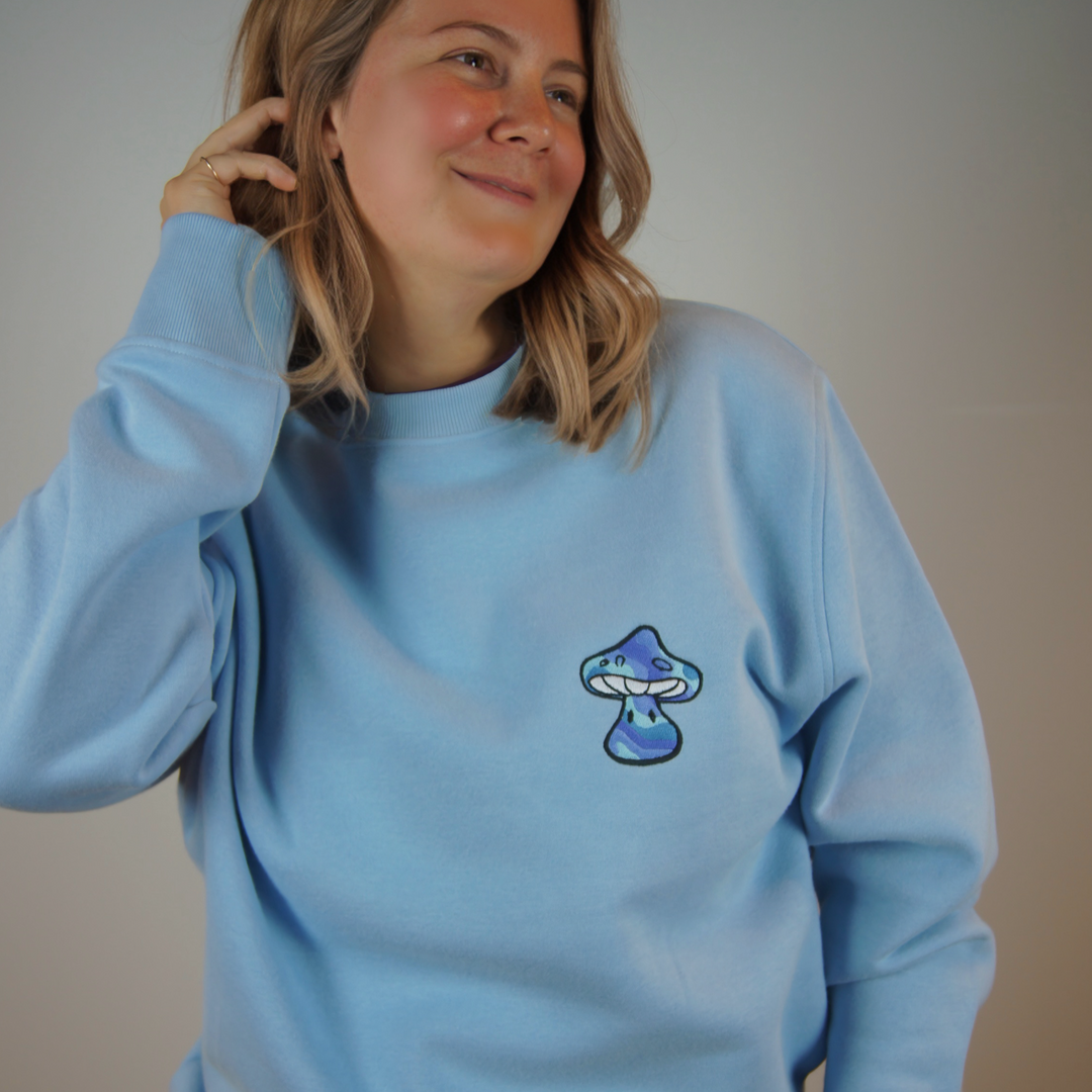 Person wearing a light blue sweatshirt with a mushroom design on a plain background