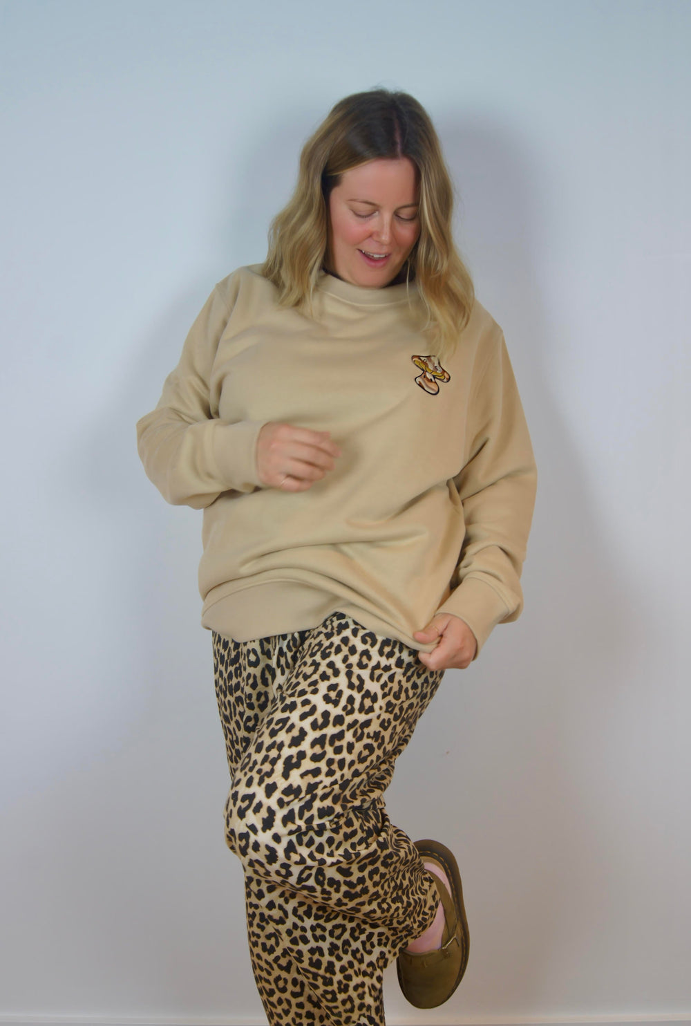 Person wearing a beige sweater and leopard print pants against a plain background