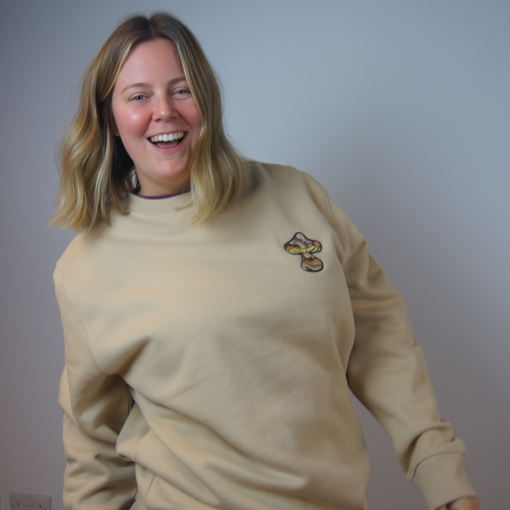 Person wearing a beige sweatshirt with a small logo and a leopard print skirt, standing against a plain background.