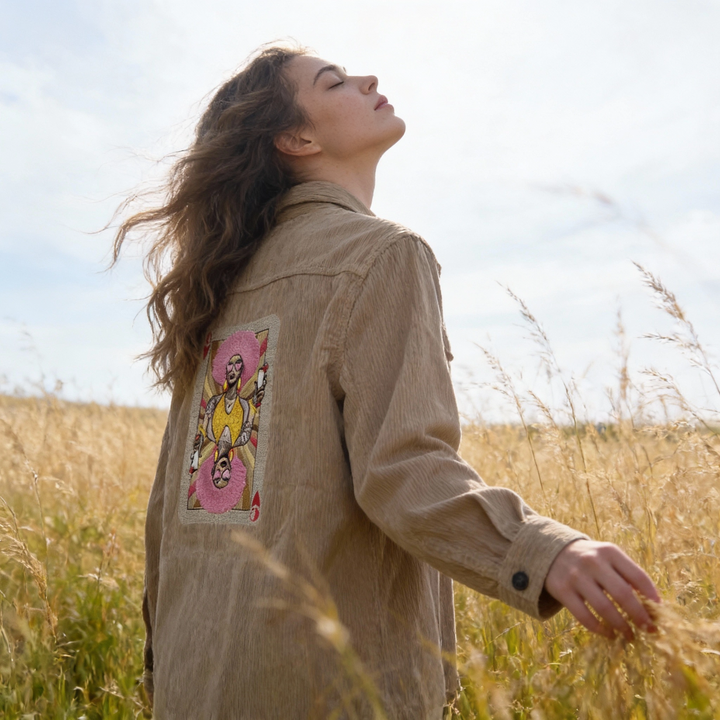 Woman standing in a field wearing a beige jacket with a colorful patch on the back.