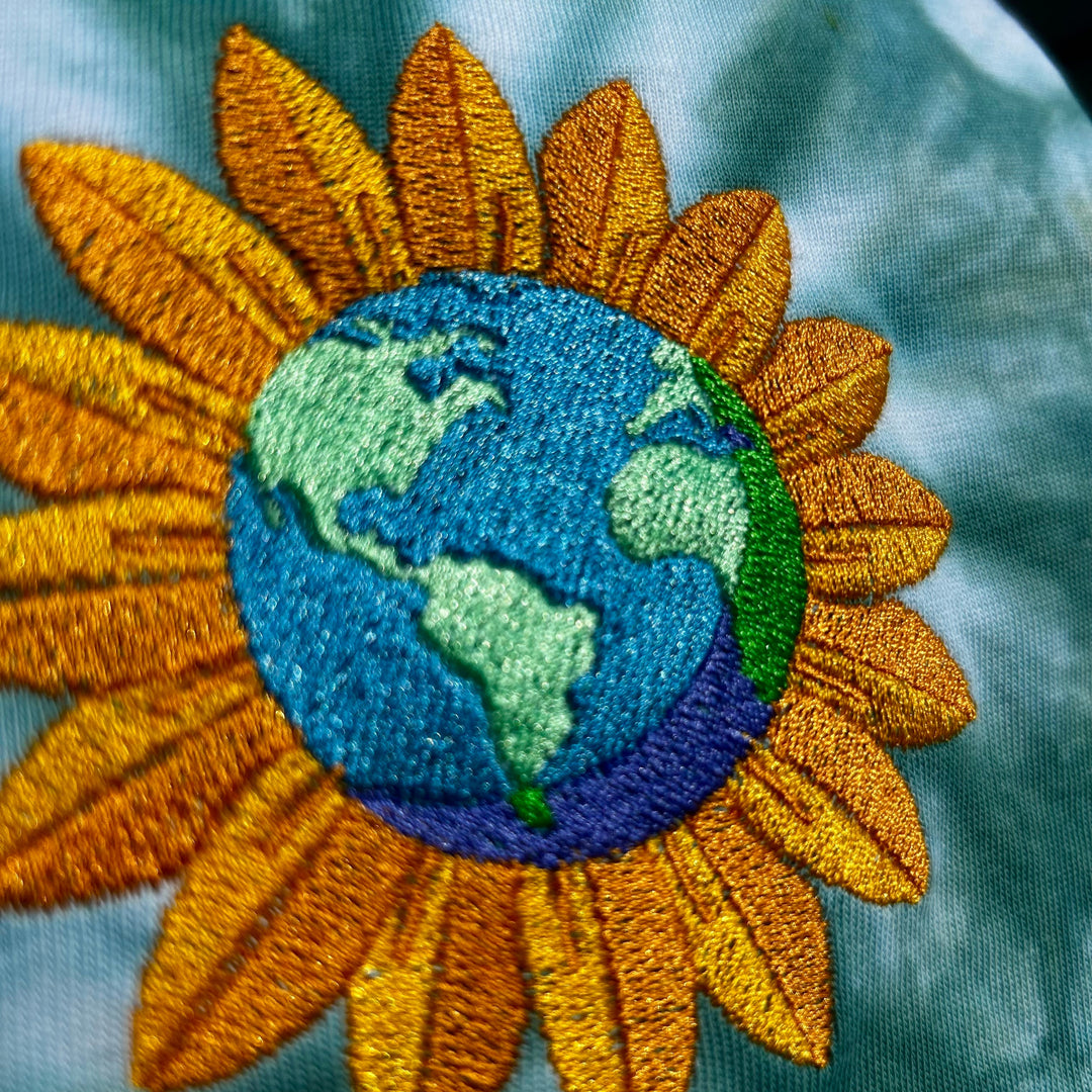 Embroidered patch of a sunflower with Earth in the center on a textured fabric background
