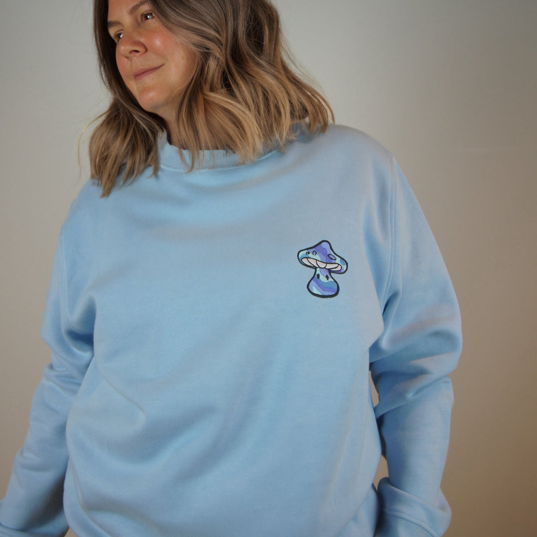 Person wearing a light blue sweatshirt with a small graphic on a plain background