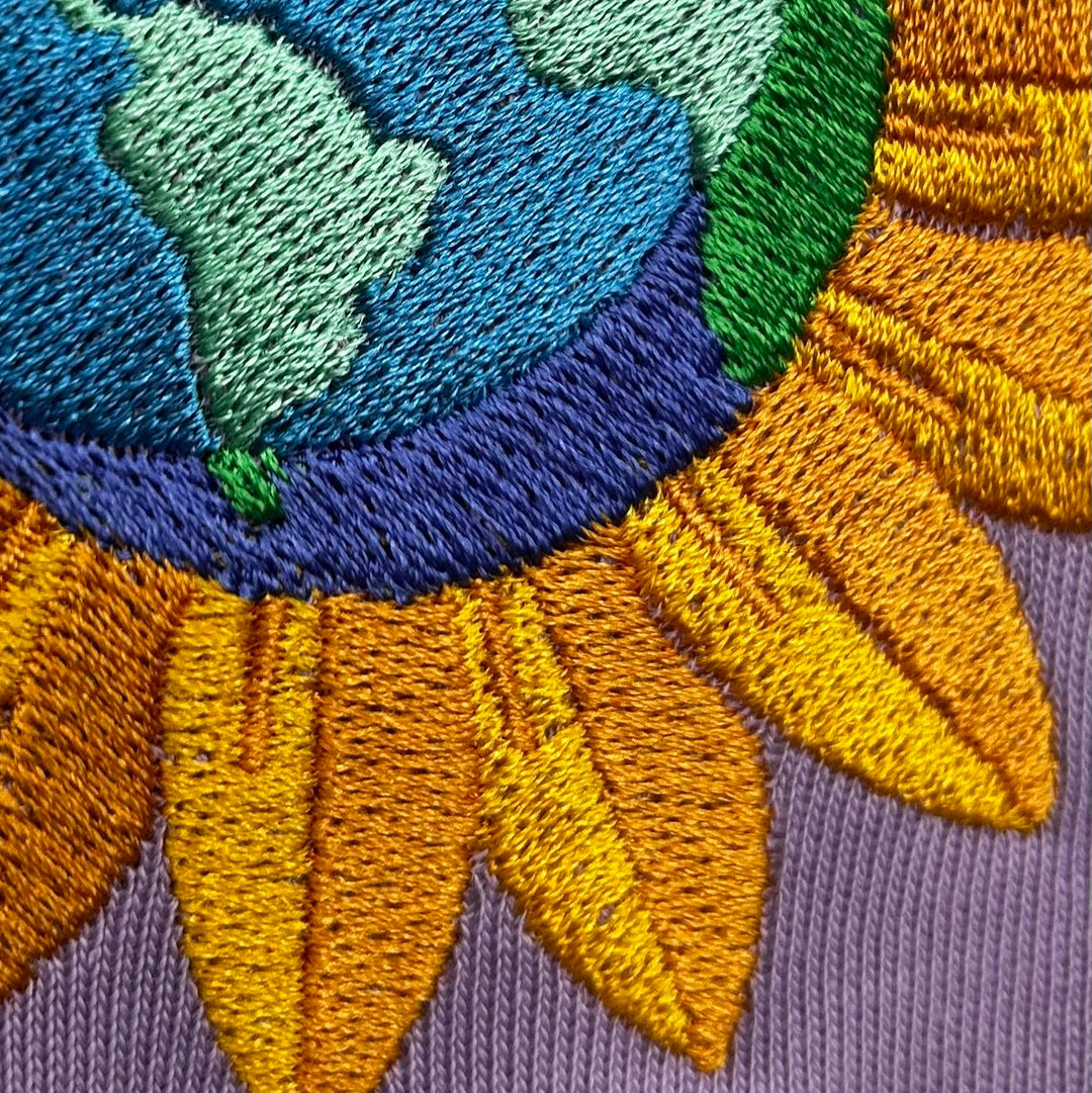 Close-up of embroidered design with blue, green, and orange colors on a purple fabric background.