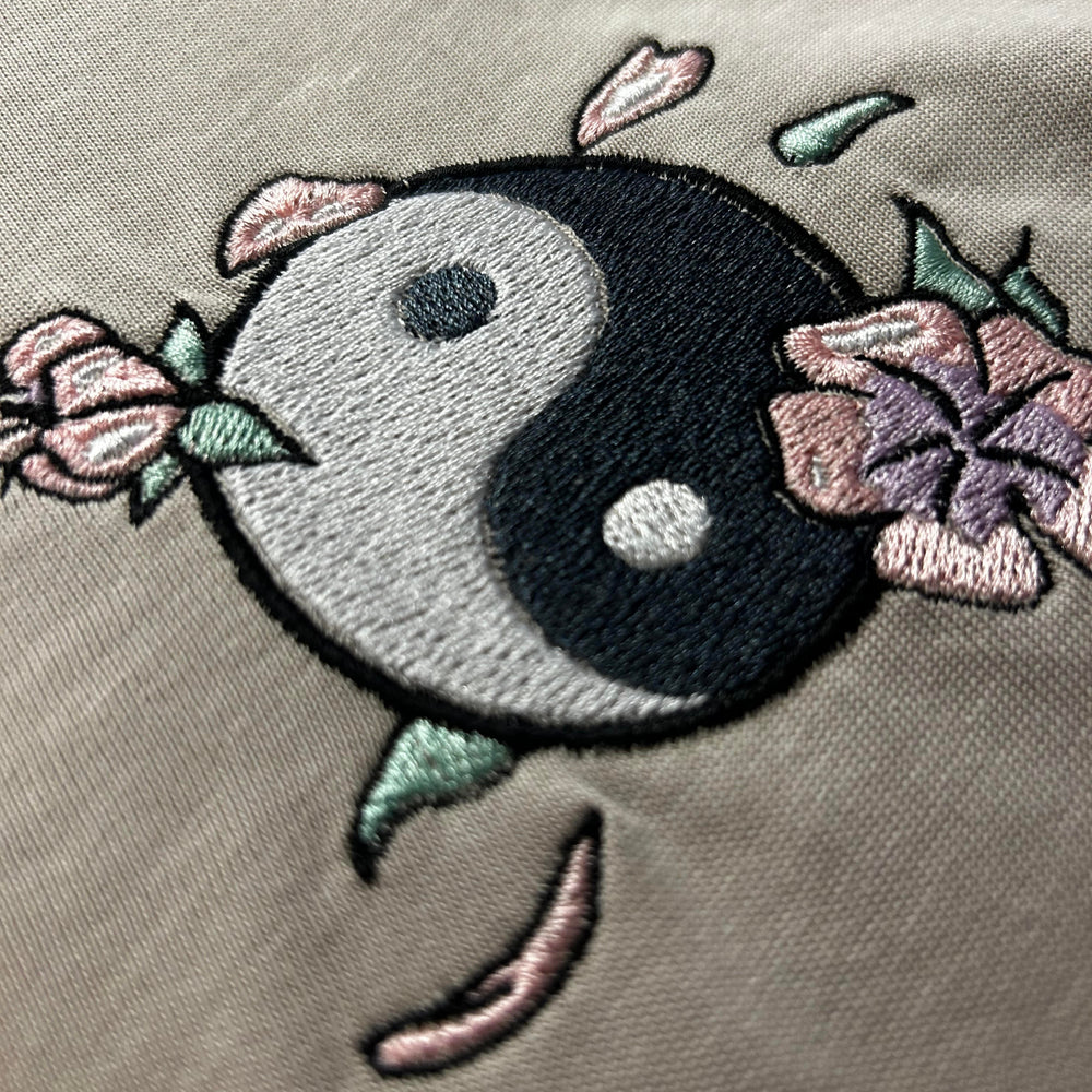 Embroidered yin yang symbol with floral elements on a beige fabric background