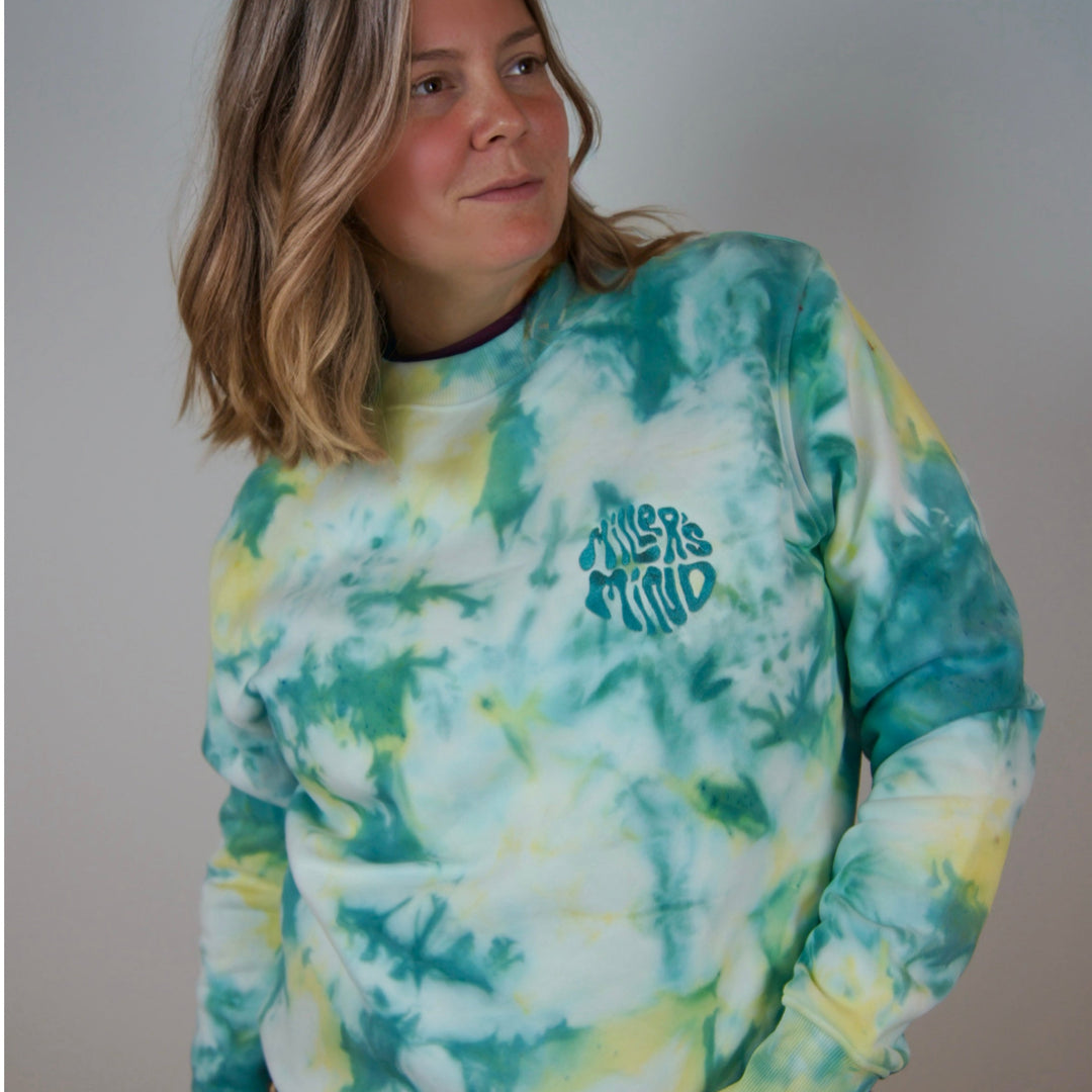 Person wearing a tie-dye sweatshirt with text and leopard print pants against a plain background
